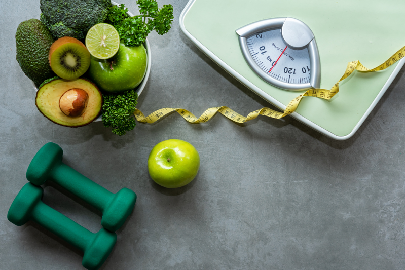 weight loss scale, green weights, and vegetables on gray background